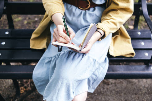 Frau schreibt Tagebuch, während sie auf einer Bank sitzt - ASGF01642