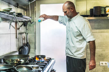 Männlicher Koch gießt Öl in eine Pfanne im Restaurant - DLTSF02302