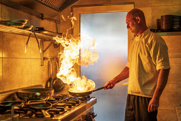 Männlicher Koch mit flammender Pfanne beim Kochen in der Küche - DLTSF02303