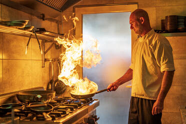 Male chef with flaming pan cooking in kitchen - DLTSF02303