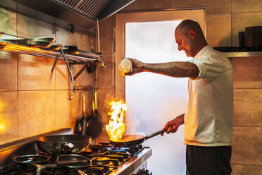 Male chef with burning flame pouring oil in pan - DLTSF02305