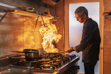 Male chef holding pan while cooking in restaurant - DLTSF02314