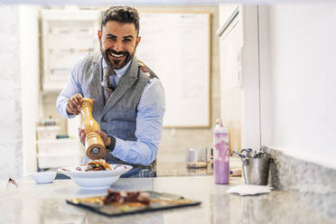 Lächelnder männlicher Koch mit Pfeffermühle am Küchentisch - DLTSF02318