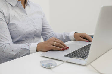 Businesswoman sitting at desk and working on laptop in home office - MOMF00938