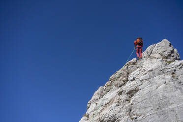 Männlicher Bergsteiger beim Klettern auf den Alpi Apuane mit Seil vor einem klaren Himmel - MCVF00915