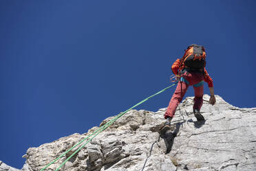 Älterer Mann klettert mit Seil an einem sonnigen Tag einen Berg hinauf - MCVF00916