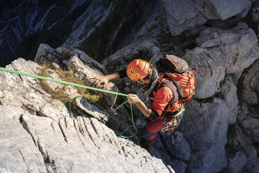 Entschlossener männlicher Wanderer, der sich an einem sonnigen Tag mit einem Seil vom Berg abseilt - MCVF00917