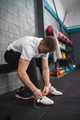 Young male athlete tying shoelace in gym - SNF01517
