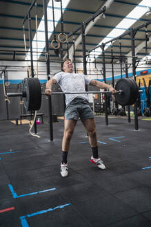 Motivierter männlicher Sportler, der eine Langhantel hebt, während er im Fitnessstudio trainiert - SNF01529
