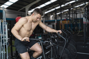 Männlicher Sportler ohne Hemd trainiert auf einem Crosstrainer im Fitnessstudio - SNF01534