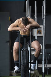 Exhausted sportsman resting on cross trainer in gym - SNF01538