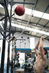 Hemdloser Sportler wirft Sportball beim Training im Fitnessstudio - SNF01548