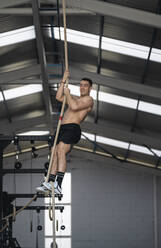 Lächelnder Sportler, der mit einem Seil im Fitnessstudio trainiert - SNF01552