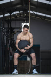 Entschlossener männlicher Sportler, der einen Hantelsack hält, während er im Fitnessstudio trainiert - SNF01556
