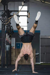 Shirtless sportsman practicing handstand while working out in gym - SNF01561