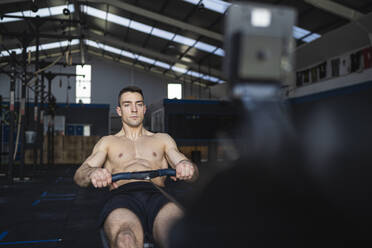 Shirtless sportsman exercising on rowing machine in gym - SNF01566