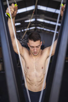 Shirtless male athlete standing by exercise machine in gym - SNF01567