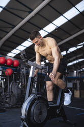 Motivated male athlete exercising on exercise bike in gym - SNF01568