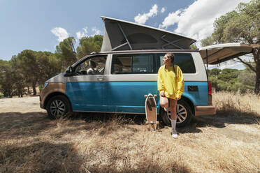 Young woman leaning on camper van on sunny day - MRRF01631