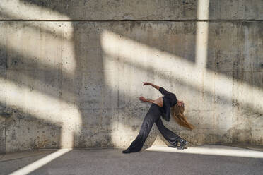Carefree woman dancing by wall on sunny day - RDGF00359