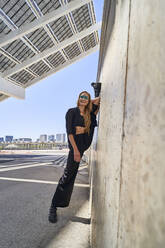 Smiling woman with leg up by wall on sunny day - RDGF00361
