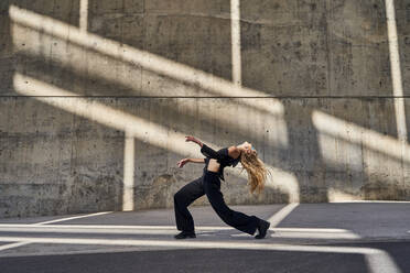 Carefree blond woman dancing on street by wall - RDGF00364