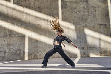 Woman with hair toss dancing on street in front of wall - RDGF00365
