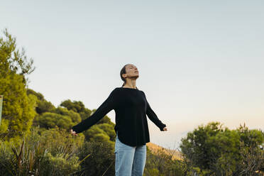 Woman with arms outstretched standing by plants - DMGF00559