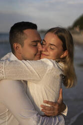 Smiling couple with eyes closed embracing at beach - SSGF00093