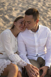Young woman leaning over boyfriend's shoulder while sitting on sand - SSGF00094