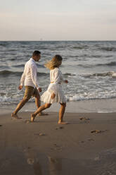 Couple running by sea at beach on sunset - SSGF00096