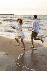 Playful couple running on sand by sea at beach - SSGF00098