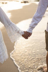 Young couple holding hands at beach on sunset - SSGF00099