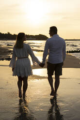 Boyfriend and girlfriend holding hands while walking at beach on sunset - SSGF00100