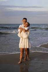 Young boyfriend embracing girlfriend in front of sea at beach - SSGF00107