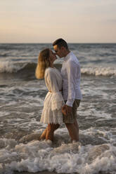 Couple rubbing nose while standing in sea on sunset - SSGF00108