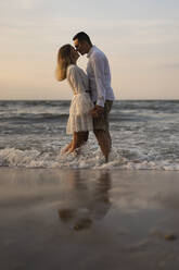 Young couple rubbing nose while standing in sea at beach - SSGF00109