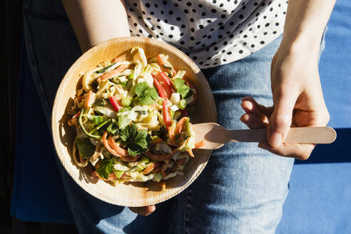 Mid section of woman eating bowl of raw vegan pad thai - EVGF03920