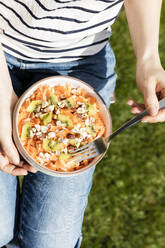 Mid section of woman eating bowl of fruit salad - EVGF03932