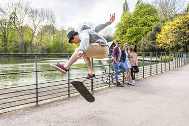 Junger Mann zeigt Freunden im Park einen Stunt auf dem Skateboard - WPEF05457