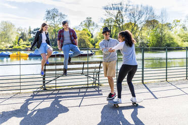 Mann bringt einem Freund an einem sonnigen Tag das Skateboardfahren bei - WPEF05462