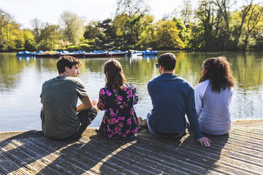 Freunde sitzen nebeneinander an einem Teich im Park - WPEF05470