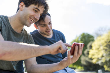 Mann teilt Smartphone mit Freund im Park - WPEF05478