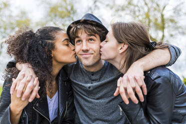 Young women with eyes closed kissing cheeks of smiling man - WPEF05498