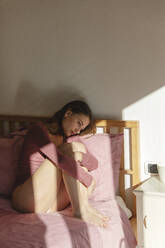 Depressed woman hugging knees on bed at home - MRAF00656