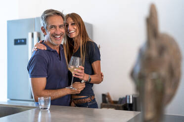 Happy couple with wineglass standing in kitchen at home - DLTSF02340