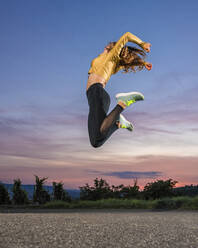 Junge Frau springt in der Abenddämmerung beim Sport gegen den Himmel - STSF03048