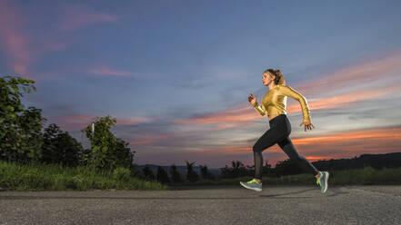 Junge Frau joggt allein in der Abenddämmerung - STSF03049
