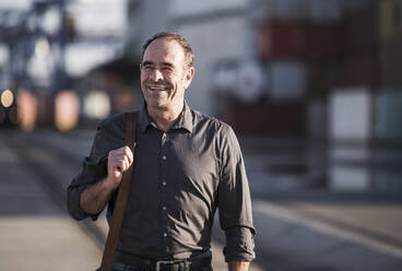 Smiling businessman with shoulder bag walking on street - UUF24937