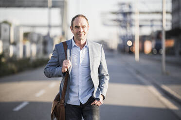 Confident businessman with shoulder bag walking on street - UUF24943